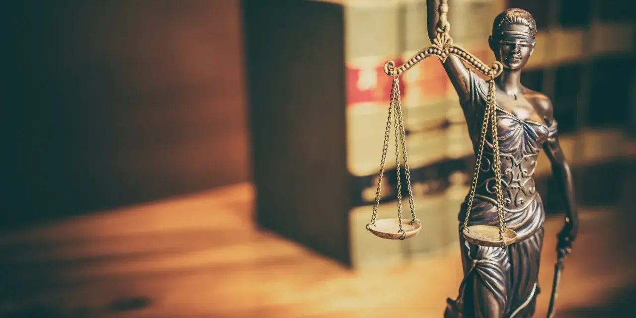 Temida z wagą i mieczem, symbol sprawiedliwości, na tle książek. Jej postawa sugeruje odrzucenie wniosku o wstrzymanie wykonania kary.