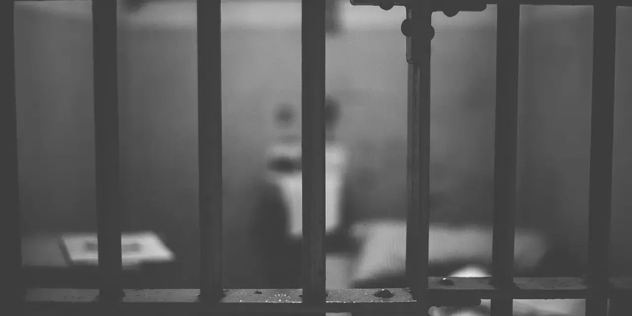 Widok przez kraty więzienne. Ciemne, ponure wnętrze celi, symbolizujące karę pozbawienia wolności.