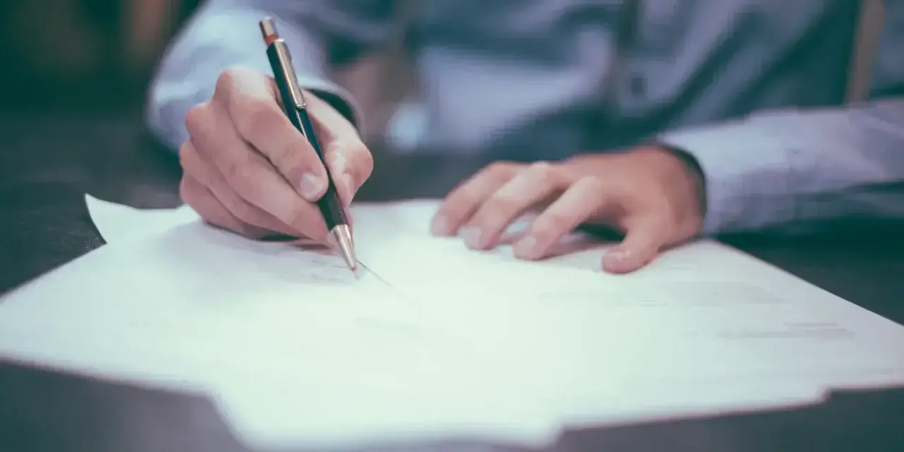 Dłoń pisze długopisem na papierze. Może to być wniosek o obrońcę z urzędu.
