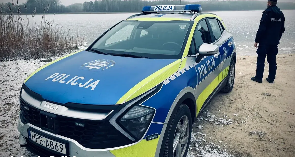 Policyjna lodówka stoi nad zamarzniętym jeziorem. Policjant w mundurze obserwuje okolicę.