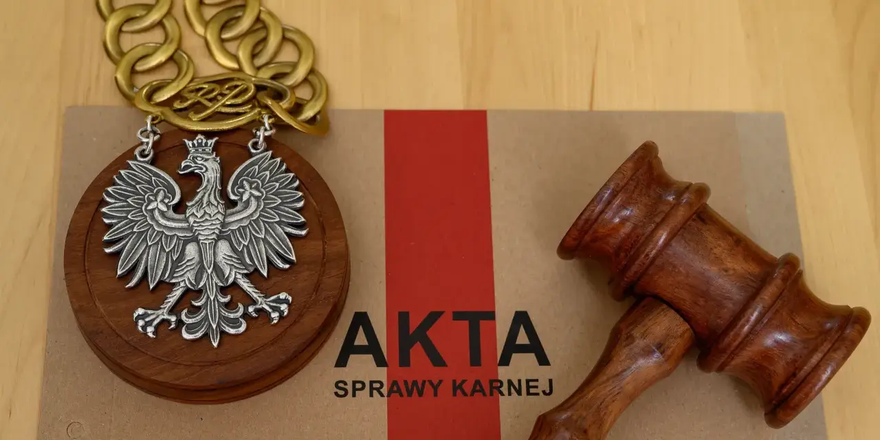 Na brązowej teczce z napisem "AKTA SPRAWY KARNEJ" leży drewniany młotek sędziowski i medalion z orłem RP.