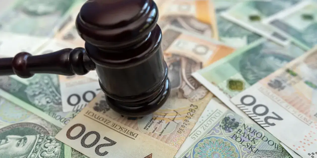 Młotek sędziowski na stosie polskich banknotów. Określenie "stawka dzienna kk" może sugerować koszty sądowe lub kary finansowe.