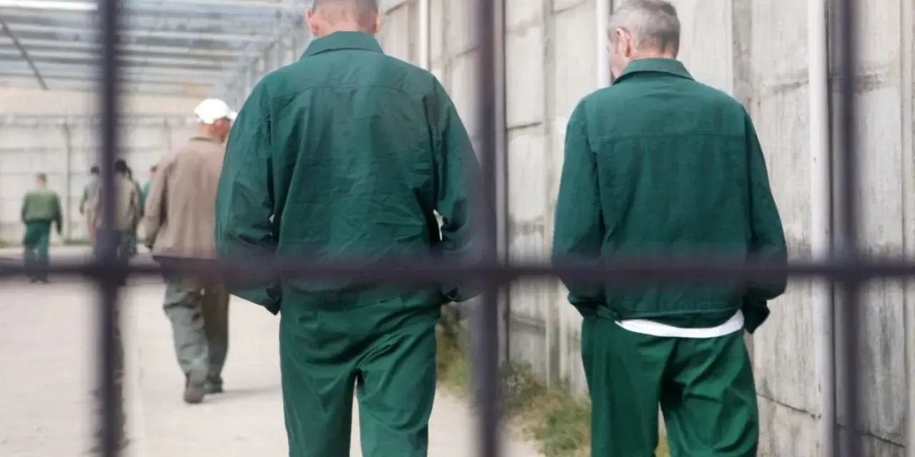 Dwóch mężczyzn w zielonych strojach więziennych w Polsce idzie korytarzem.
