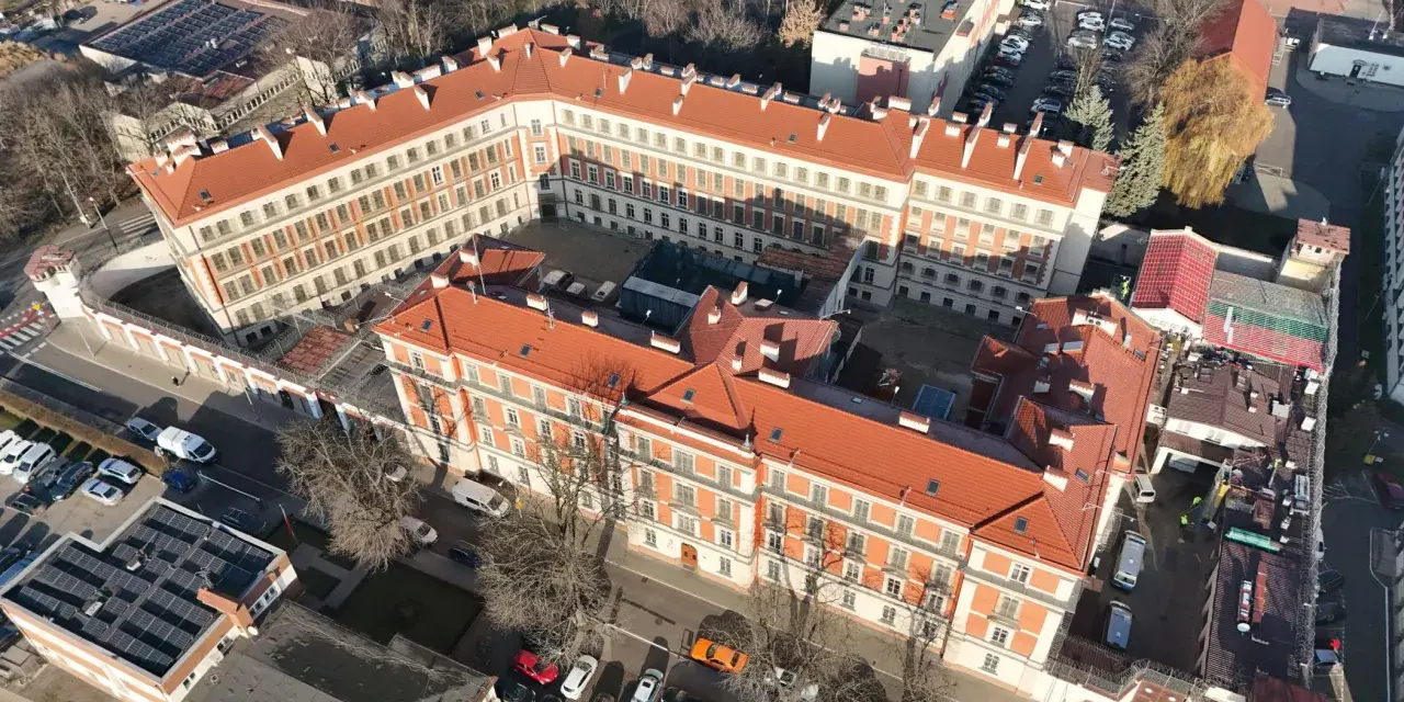 Widok z lotu ptaka na budynki więzienia aś montelupich. Czerwone dachy, białe fasady, dziedziniec z samochodami i drzewami.