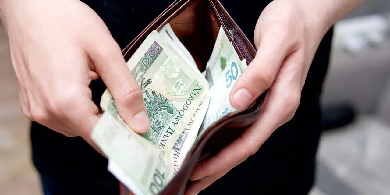 Dłonie wkładają polskie banknoty do portfela. Może to symbolizować rekompensatę za nękanie, która wreszcie trafia do poszkodowanego.
