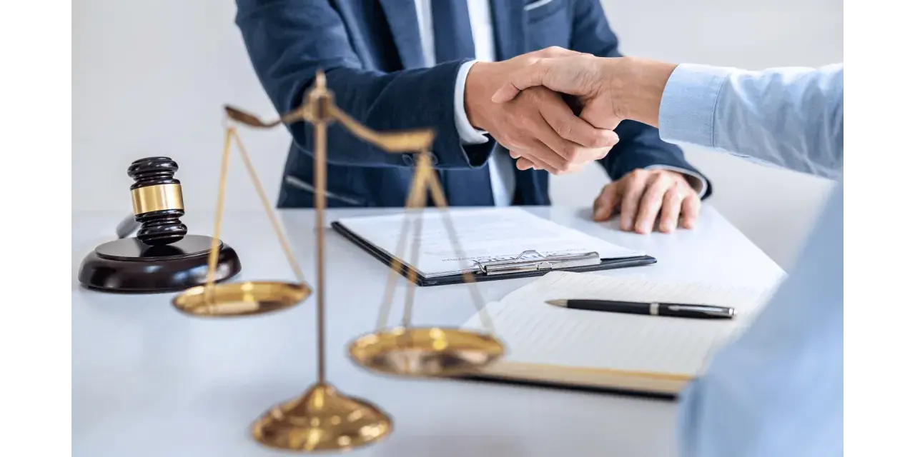 Uścisk dłoni prawników przy biurku z wagą sprawiedliwości i młotkiem. Sprawa 157 kk zakończona sukcesem.