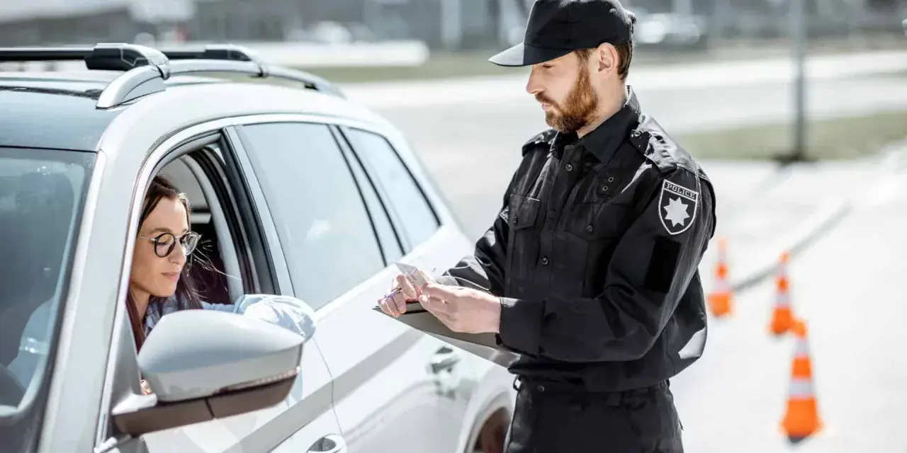 Policjant spisuje dane kierowcy, który może być zagrożony **przepadkiem pojazdu**. Kobieta w okularach siedzi za kierownicą białego samochodu.