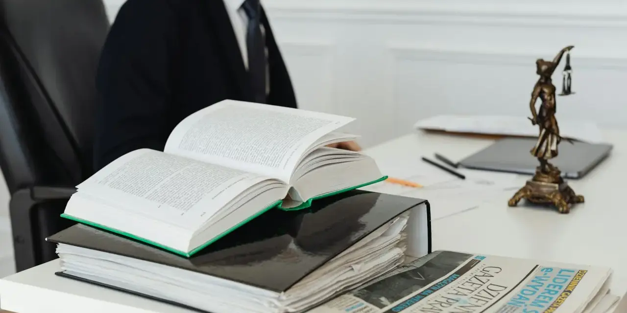 Prawnik w garniturze studiuje kodeks, art. 11 kpk, obok stosu akt i gazety "Dziennik Gazeta Prawna".