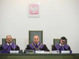 Trzech sędziów w togach podczas jawnego posiedzenia sądu. Na ścianie wisi godło Polski.