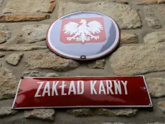 Tablica z napisem "ZAKŁAD KARNY" i godło Polski na kamiennej ścianie.