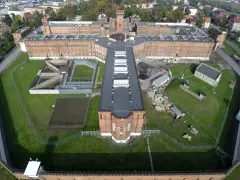Widok z lotu ptaka na zakład karny typu zamkniętego. Czerwone ceglane mury, wieża zegarowa, dziedzińce i tereny zielone otoczone ogrodzeniem z drutem kolczastym.