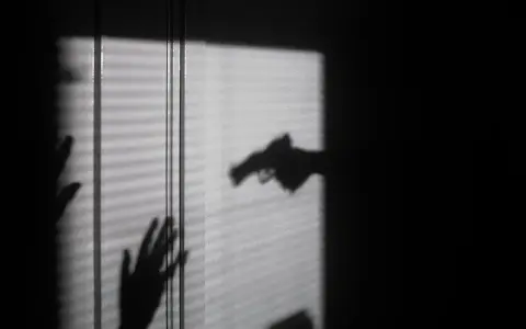 Cień dłoni z pistoletem grozi dwóm dłoniom, które próbują się zasłonić. To scena jak z filmu o świadku koronnym.