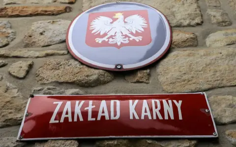 Tablica z napisem "ZAKŁAD KARNY" i godło Polski na kamiennej ścianie.