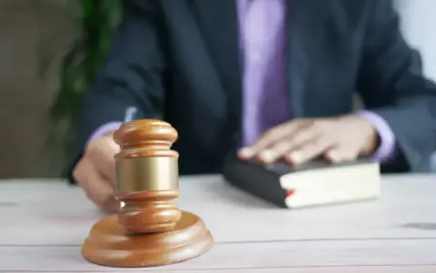 Sędzia kładzie rękę na księdze, obok młotka. Czas oczekiwania na uprawomocnienie wyroku karnego może być różny.