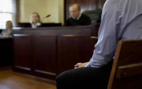 Osoba siedzi w ławie sądowej, czekając na decyzję w sprawie zgodnej z art. 37a. Sąd obraduje.