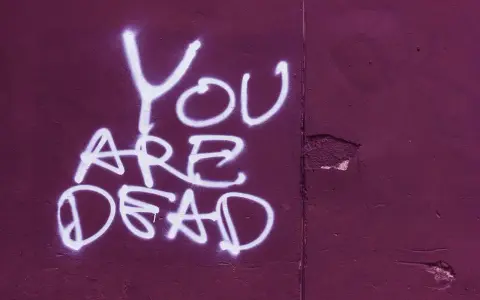 Napis "YOU ARE DEAD" białą farbą na fioletowej ścianie. Groźba jak z artykułu 190 paragraf 1 kk.