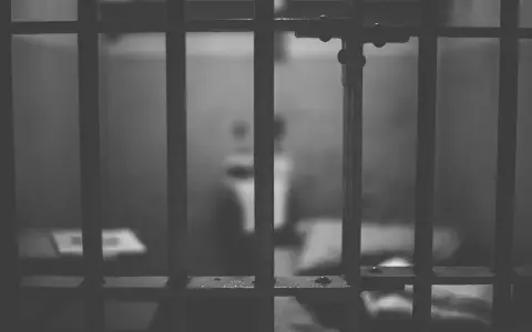 Widok przez kraty więzienne. W tle niewyraźna postać, symbolizująca nadzieję na wcześniejsze zatarcie skazania i nowe życie.