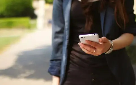 Kobieta z telefonem w dłoni, być może szuka przykładów uporczywego nękania w internecie.