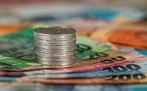 Stos monet na kolorowych banknotach. W tle widoczne fragmenty banknotów o nominałach 100 i 200, co może nawiązywać do artykułu 278 kpk.