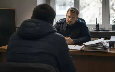 Policjant w mundurze rozmawia z mężczyzną w kurtce. Na biurku stosy dokumentów, jakby przygotowywano komentarz do art. 284 par. 2 kk.