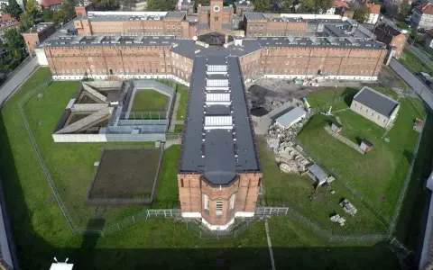 Widok z lotu ptaka na zakład karny typu zamkniętego. Czerwone ceglane mury, wieża zegarowa, dziedzińce i tereny zielone otoczone ogrodzeniem z drutem kolczastym.