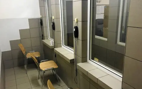 Pokój widzeń w zakładzie karnym półotwartym. Proste krzesła i telefony czekają na rozmowy.
