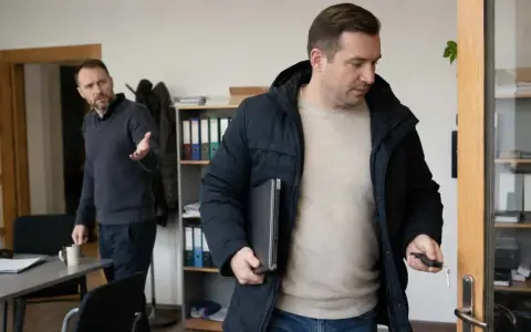 Mężczyzna wychodzi z biura z laptopem pod pachą, trzymając kluczyki. Jego kolega gestykuluje, sugerując przywłaszczenie mienia.