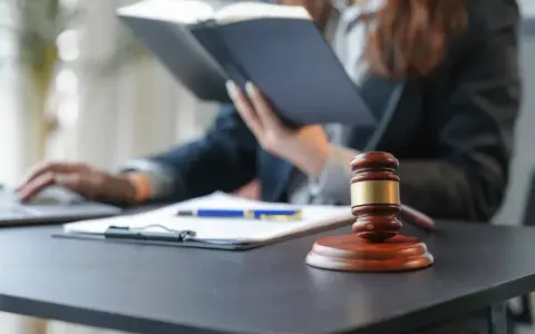 Sądowy młotek i dokumenty na biurku. Prawnik w tle studiuje akta, zastanawiając się, czy radca prawny może być obrońcą.