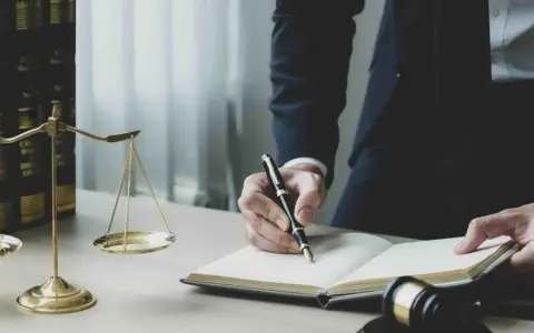 Prawnik pisze notatki do sprawy, obok wagi sprawiedliwości i ksiąg prawnych.