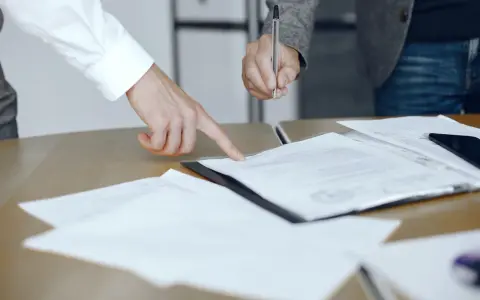 Dwie osoby przy biurku analizują dokumenty. Jedna wskazuje palcem na tekst, druga trzyma długopis, gotowa do podpisania. To może być moment, gdy omawiają, co to jest list żelazny.