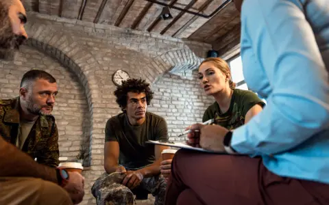 Grupa żołnierzy na terapii. Kobieta w mundurze mówi, mężczyźni słuchają. Może to najbardziej luksusowe więzienie na świecie?