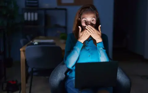 Kobieta zszokowana treścią na laptopie, czuje się jakby była obiektem prześladowania kogoś.