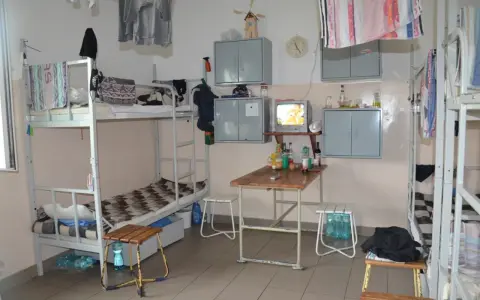 Wnętrze przypomina **zakład karny cela** z łóżkami piętrowymi, stołem, telewizorem i szafkami.