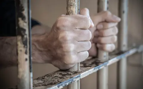 Dłonie więźnia zaciskają się na kratach. Może to być symbol nadziei na zwolnienie, gdy przygotowuje wniosek do dyrektora zakładu karnego wzór.