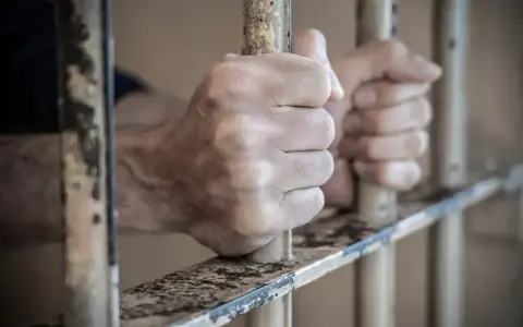 Dłonie zaciskają się na kratach więziennych. Dowiedz się, jak skontaktować się z osadzonym, szukając informacji o odwiedzinach i korespondencji.