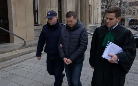 Policjant eskortuje podejrzanego przed budynkiem sądu. Ile jest więzień w Polsce? To pytanie nurtuje wielu.