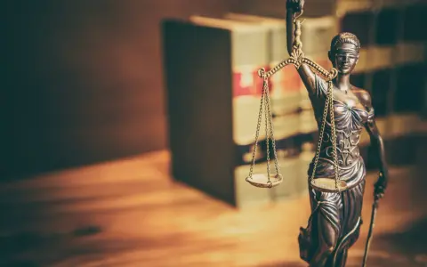 Temida z wagą i mieczem, symbol sprawiedliwości, na tle książek. Jej postawa sugeruje odrzucenie wniosku o wstrzymanie wykonania kary.