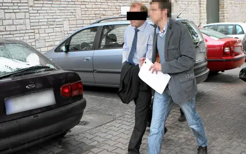Dwóch mężczyzn, jeden w garniturze, drugi w kurtce i jeansach, idzie obok samochodów. Czy to występek, co to za sytuacja?