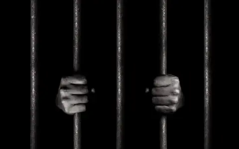 Dwie dłonie zaciskają się na kratach więziennych. To obraz symbolizujący nadzieję na wolność i wzór wniosku o przepustkę z zakładu karnego.
