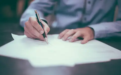 Dłoń pisze długopisem na papierze. Może to być wniosek o obrońcę z urzędu.