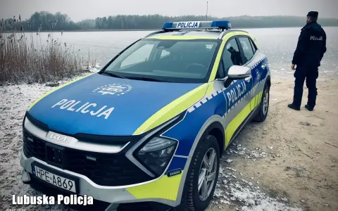 Policyjna lodówka stoi nad zamarzniętym jeziorem. Policjant w mundurze obserwuje okolicę.