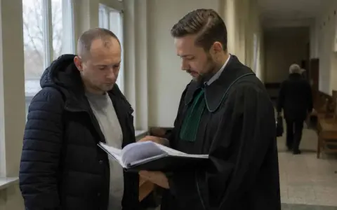 Prawnik w todze pokazuje klientowi dokumenty. Rozmawiają o wniosku o naprawienie szkody kpk.