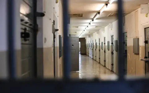 Korytarz więzienny z rzędami cel po obu stronach, widok przez kraty.