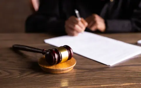 Młotek sędziowski na drewnianym stole, w tle osoba pisząca dokumenty. Symbolizuje postępowanie wykonawcze.