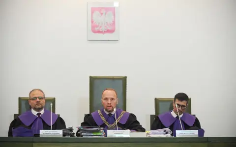 Trzech sędziów w togach podczas jawnego posiedzenia sądu. Na ścianie wisi godło Polski.