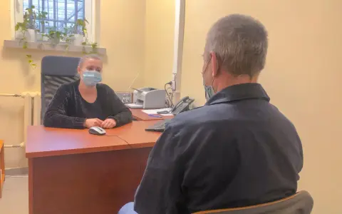 Psycholog więzienny w masce rozmawia z osadzonym. W tle okno z kratami i rośliny.