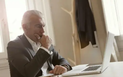 Biznesmen w garniturze zamyślony nad laptopem, przygotowuje się do wszczęcia śledztwa.