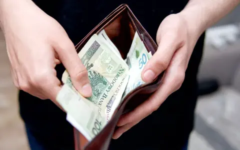 Dłonie wkładają polskie banknoty do portfela. Może to symbolizować rekompensatę za nękanie, która wreszcie trafia do poszkodowanego.