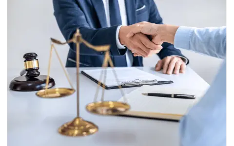 Uścisk dłoni prawników przy biurku z wagą sprawiedliwości i młotkiem. Sprawa 157 kk zakończona sukcesem.
