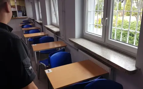 Rzędy pustych ławek i krzeseł w sali lekcyjnej. Za kratami okien widać zieleń. To może być sala egzaminacyjna w więzieniu na Białołęce.